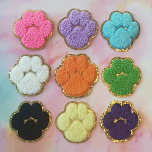 May include: Nine felt paw print patches in various colors, including pink, purple, blue, white, orange, green, black, yellow, and purple. Each patch has a gold glitter outline.