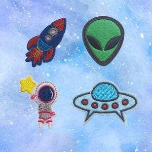 May include: Four embroidered iron-on patches with a space theme. The patches include a rocket, an alien, an astronaut holding a star, and a flying saucer.