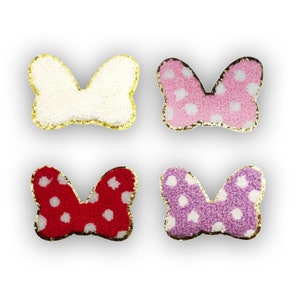 May include: Four fuzzy fabric bows with gold trim. The bows are in white, pink, red, and purple with white polka dots.