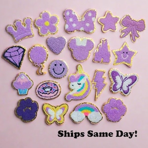 May include: A collection of purple embroidered patches in various shapes, including a crown, flower, bow, star, heart, and a smiling face. The patches have gold trim and are on a pink background. Text at the bottom reads "Ships Same Day!"