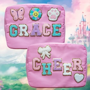 May include: Two pink cosmetic bags with decorative patches. One bag has a butterfly, flower, and paw print patch, with the name "GRACE" in colorful letters. The other bag has a bow, heart, and the name "CHEER".