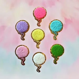 May include: Seven colorful fuzzy balloon shaped iron-on patches with gold glitter accents. The balloons are pink, purple, yellow, blue, green, white, and light pink.