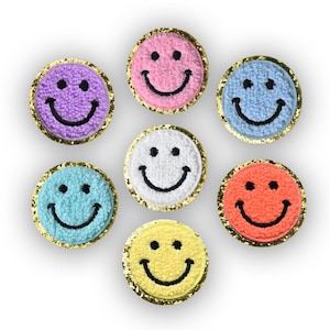 May include: Seven colorful smiley face patches. Each patch features a different color, including purple, pink, blue, teal, white, orange, and yellow. The smiley faces are embroidered with black thread and have a gold glitter border.
