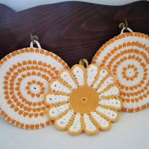 May include: Three crocheted pot holders in white and orange. Two are round and one is a flower shape.