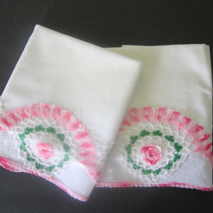 May include: Two white pillowcases with pink and green crocheted lace trim. The lace features a floral design with a pink rose in the center.