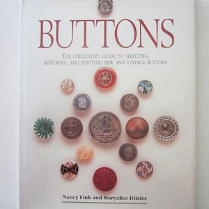 May include: A book cover titled "BUTTONS" with various vintage buttons arranged around the title. The text reads "The Collector's Guide to Selecting, Restoring, and Enjoying New and Vintage Buttons." Authors are Nancy Fink and Maryalice Ditzler.