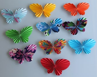May include: A collection of 10 colourful paper butterflies, each with a unique design and pattern. The butterflies are arranged in a random pattern on a light blue background.