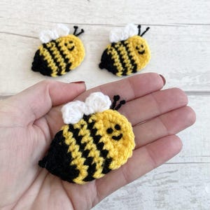 May include: Three crocheted bumblebees with black and yellow stripes, white wings, and smiling faces.