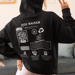 May include: Black hoodie with a white graphic design that says "Dog Walker" and includes a QR code, a paw print, and a list of "ingredients" needed to be a dog walker. The text includes "Endless energy, love for animals, patience, reliability, communication skills, quick reflexes, problem-solving, empathy, time management, route planning expertise, leash-handling skills, weather resilience, and a big heart."