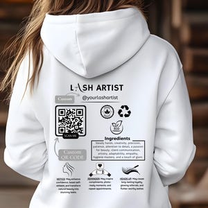 May include: White hoodie with a black and white design featuring the text "LASH ARTIST @yourlashartist", a QR code, and the words "Custom QR Code". The hoodie also has a graphic of a lash and the text "Ingredients" with a list of qualities needed to be a lash artist.