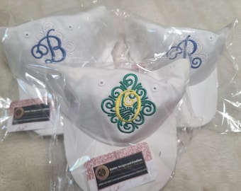 May include: Three white baseball caps with embroidered designs. One cap has a blue letter B, another has a blue letter R, and the third has a green and yellow floral design with a yellow letter O in the center.