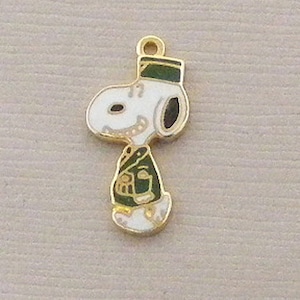 May include: Gold-tone metal charm featuring a cartoon image of Snoopy dressed as a soldier. Snoopy is wearing a green uniform and a hat.