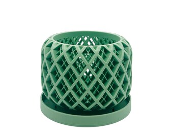 May include: A sage green, cylindrical planter with a diamond lattice design. The planter sits on a matching round base. The openwork design allows for air circulation and drainage, suitable for small plants or succulents.