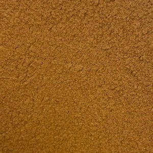 May include: Close-up of a textured, brown surface. The surface has a rough, granular appearance, with a consistent color and pattern across the entire image. The texture suggests a natural material.