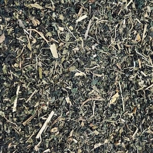 May include: Close-up of dried green herbs and plant matter. The image shows a mix of small, dark green leaves, stems, and light-colored pieces, creating a textured, natural appearance. The composition suggests a focus on herbal ingredients.
