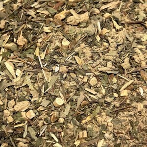 May include: Close-up of a mix of dried herbs and spices. The image shows a blend of green, brown, and tan components, including what appear to be leaves, stems, and small, irregular pieces. The texture is rough and granular.