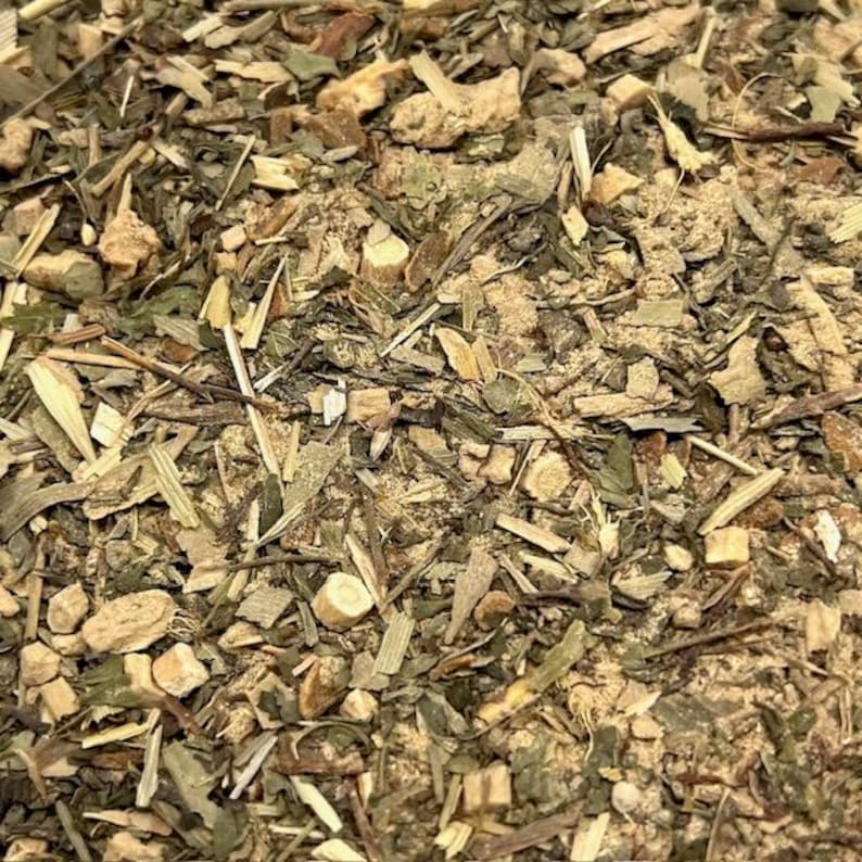 May include: Close-up of a mix of dried herbs and spices. The image shows a blend of green, brown, and tan components, including what appear to be leaves, stems, and small, irregular pieces. The texture is rough and granular.