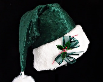 May include: A green velvet Christmas hat with a white fluffy trim. The hat features a white pom-pom and is decorated with a green ribbon, holly, and red berries. The hat is set against a black background.