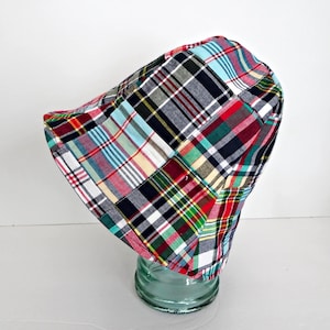 Op de afbeelding: Een patchwork emmerhoed in een levendig ruitpatroon. De hoed heeft een mix van rode, blauwe, groene en gele vierkanten, waardoor een kleurrijk en opvallend ontwerp ontstaat. De hoed is gemaakt van stof en heeft een ronde kroon en een rand.