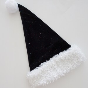 May include: A black Santa hat with a white fluffy trim and a white pom-pom at the tip. The hat is covered in tiny, colorful glitter, giving it a festive, sparkling appearance. This holiday accessory is perfect for Christmas celebrations.