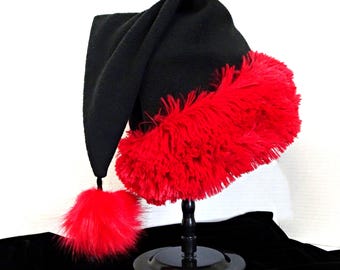 May include: A black hat with a long, pointed crown and a wide, vibrant red faux fur trim around the base. A matching red faux fur pom-pom hangs from the tip of the hat by a short black cord, creating a distinct contrast between the black and red.