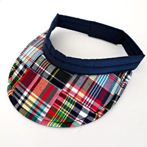 May include: A colorful plaid visor with a navy blue headband. The visor features a patchwork design with red, green, yellow, and blue squares. The headband is padded for comfort and has a curved shape.