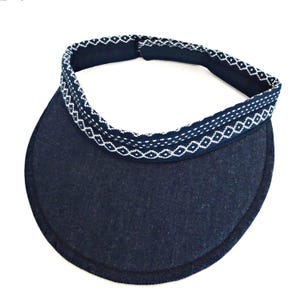 May include: A navy blue visor with a curved brim and a patterned band. The band features a repeating white geometric design. The visor is designed to shield the eyes from the sun.