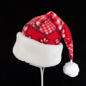 May include: A red Santa hat with a white, fluffy brim and a white pom-pom. The hat features a red and white plaid pattern with floral accents. The hat is made of a soft, fleece-like material, perfect for holiday festivities.