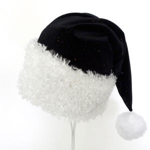 May include: A black Santa hat with a white, fluffy trim and a white pom-pom. The hat is made of a soft, velvety material and has small, colorful glitter accents. The hat is a festive accessory for the holiday season.