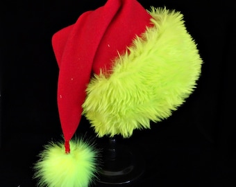 May include: A festive hat featuring a bright red felt crown and a vibrant lime green faux fur trim around the base. The hat has a long, pointed tail that hangs down to the side, finished with a matching lime green faux fur pom-pom at the tip.