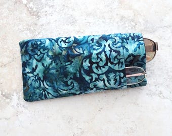 May include: A blue batik patterned glasses case holds two pairs of eyeglasses. The case is a rectangular shape with a flap closure. The glasses are visible in the case, one pair with brown frames and the other with pink frames.