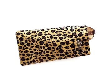 May include: A rectangular eyeglasses case featuring a tan and black leopard print pattern. The case is constructed with a slip-in opening on the right side, through which the brown frame and metal bridge of a pair of eyeglasses are partially visible.