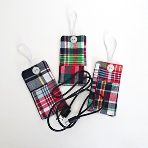 May include: Three plaid fabric cord organizers in red, green, blue, and white. Each has a white button closure and a white loop. A black charging cable is placed between the organizers.