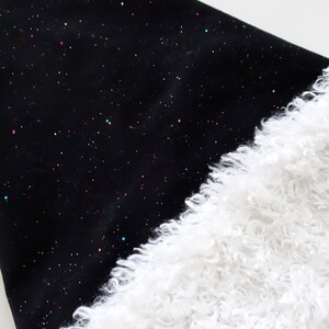 May include: Black fabric with a constellation of colorful glitter dots, paired with a fluffy white faux fur trim. The contrasting textures and colors create a visually appealing design. The fabric has a soft, slightly textured appearance.