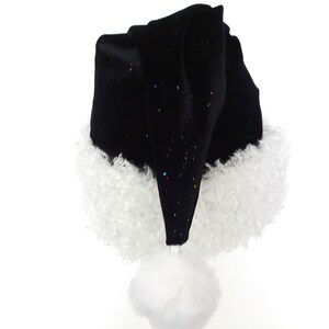 May include: A black Santa hat with a white fluffy trim and a white pom-pom. The hat is made of a soft, velvety material and has small, colorful glitter accents. The hat is a festive accessory for the holiday season.