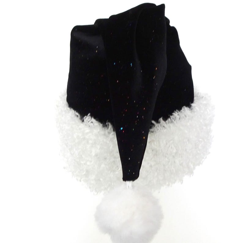 May include: A black Santa hat with a white fluffy trim and a white pom-pom. The hat is made of a soft, velvety material and has small, colorful glitter accents. The hat is a festive accessory for the holiday season.