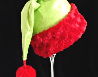 May include: A bright lime green velvet hat with a long, pointed, drooping top. The base of the hat features a wide, thick band of textured, fuzzy red faux fur. A matching red fuzzy pom-pom hangs from the tip of the hat by a thin red cord.