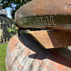 May include: Two brown kayaks stacked on a wooden rack. The top kayak has the word "TARPON" printed on the side.