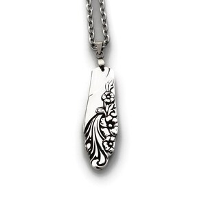 Puede incluir: Un collar de plata con un colgante de diseño floral. El colgante tiene forma de óvalo largo y estrecho y presenta un delicado patrón floral.