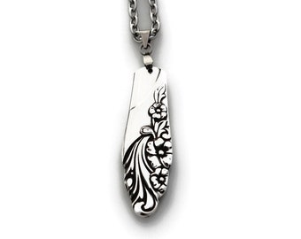 May include: A silver necklace with a floral design pendant. The pendant is shaped like a long, narrow oval and features a delicate floral pattern.