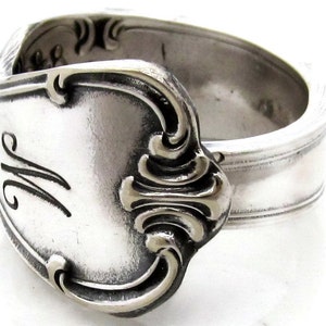 May include: A silver spoon ring with an ornate design and the letter "W" engraved on the front.