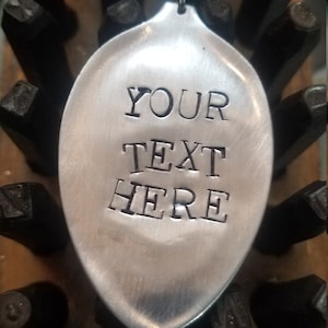 Puede incluir: Un llavero de cuchara de plata con un anillo. La cuchara tiene el texto "YOUR TEXT HERE" grabado.