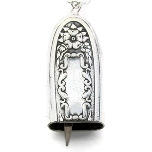 May include: A silver charm with a floral design and a blank space for engraving. The charm is shaped like a bell and has a small loop at the top for attaching to a necklace or bracelet.