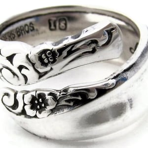 Puede incluir: Un anillo de plata en forma de cuchara con un diseño floral. El anillo está hecho de una cuchara vintage y tiene la inscripción "Rogers Bros."