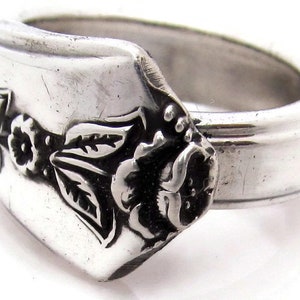 May include: A silver ring with a floral design. The ring is made from a repurposed spoon and features a rose with leaves and smaller flowers.
