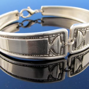 May include: Silver bracelet with a decorative design. The bracelet is made from a repurposed spoon and has a clasp closure.
