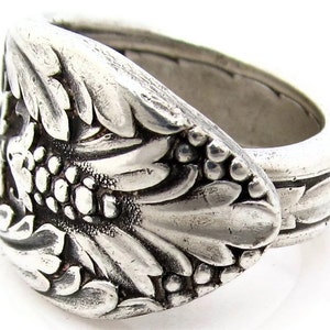 May include: A silver ring crafted from a repurposed spoon, featuring an intricate floral design. The ring is wide and has a textured finish.