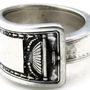 Puede incluir: Un anillo de plata en forma de cuchara con un diseño decorativo en la banda. El anillo está hecho de una cuchara reutilizada.