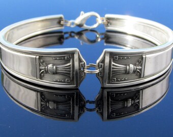May include: A silver bracelet made from a repurposed spoon. The spoon has an ornate design with a decorative floral motif.