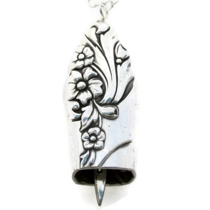 Op de afbeelding: Een zilveren ketting met een hanger met een bloemenmotief. De hanger heeft de vorm van een bel en heeft een gedetailleerd bloemenpatroon.